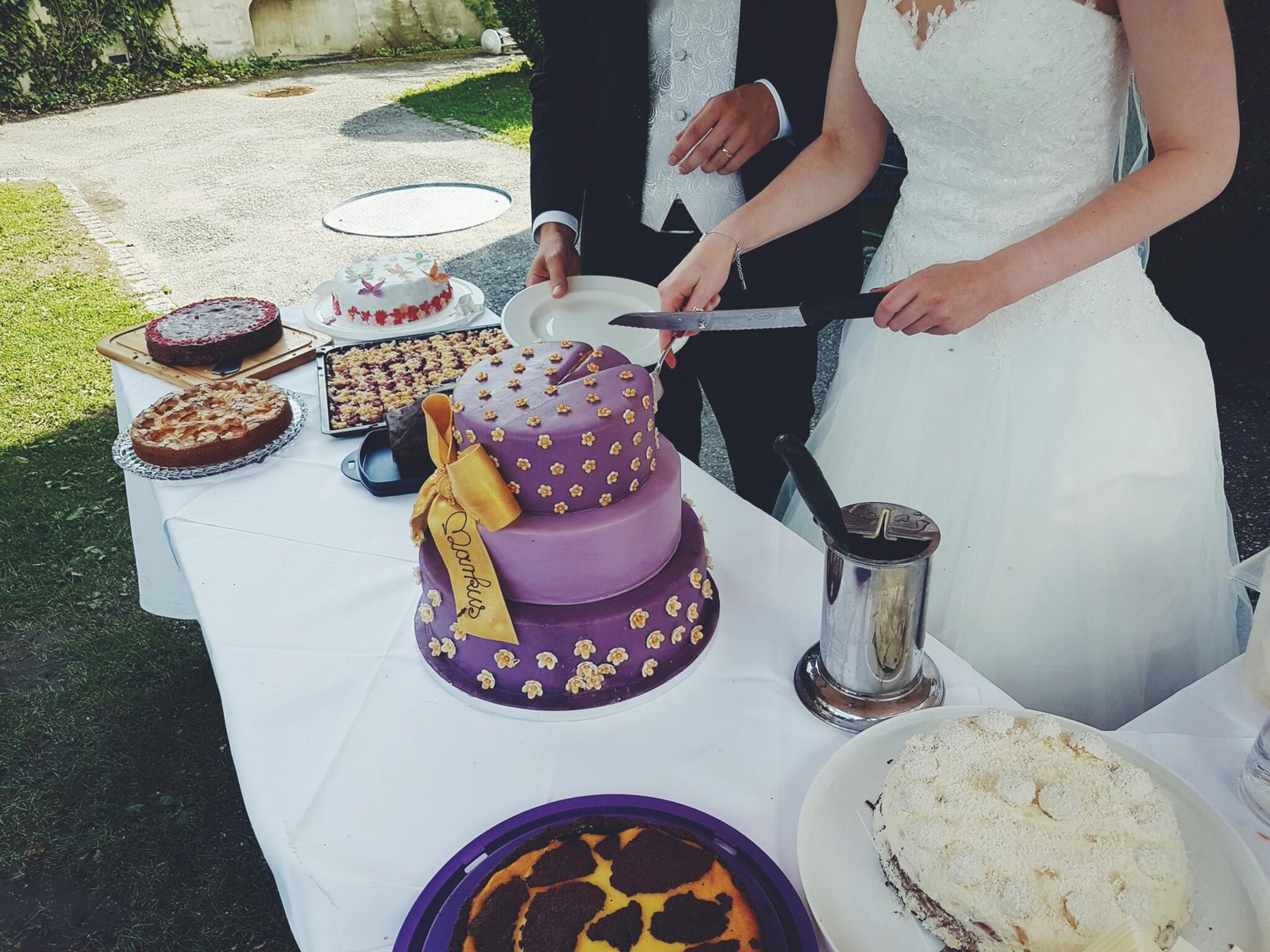 Bride and groom cutting a purple wedding cake at an outdoor celebration.